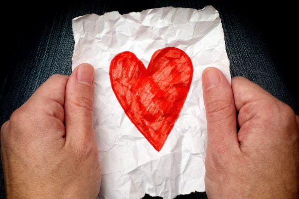 Young man holding crumpled piece of paper with red heart — Stock Photo, Image