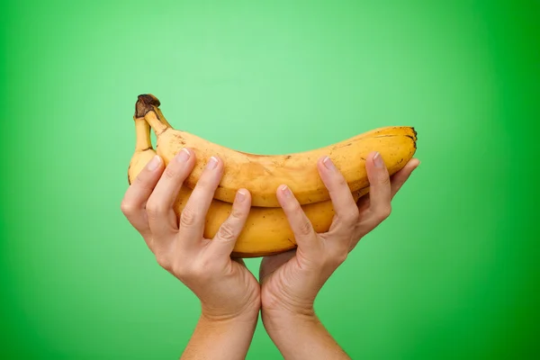 Bunch of bananas in woman hands over green background — Stock Photo, Image