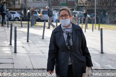 Porto, Portekiz - 26 Ekim 2020: Covid-19 salgını sırasında yüz maskesi takan yaşlı bir kadın alışveriş torbası taşırken burnuna haykırıyor. Felaket ilan edildi ve toplum içinde yüz maskesi takmak zorunludur..