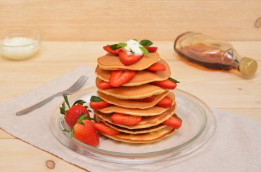 pancakes with strawberries and cream and maple syrup for them on the table