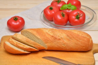 Tahtada doğranmış baget ve arkada domatesler.