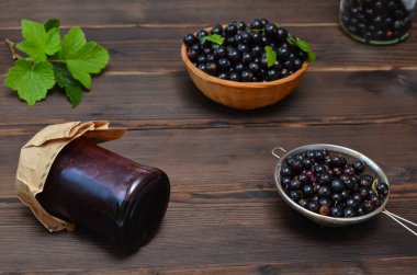 jar with jam and berries of black currant on a wooden background, rustic style