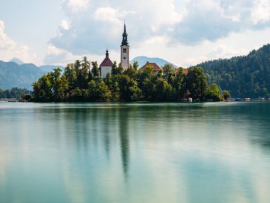 Slovenya Gölü 'ne uzun süre maruz kalma, sabahın erken saatlerinde, bulutlu bir günde, suda yansımalar, ön planda adanın yan görüntüsü, eski tarz.