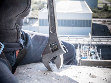 Endüstriyel bir ortamda, yüksek irtifada, koruyucu aletlerle ingiliz anahtarı olan bir işçi.