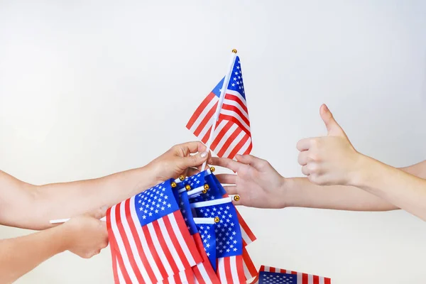 Hands pass the American flag into the hands isolated on a light background. Stars and stripes flag setting.Independence day America concept.American Flag day.Mini american Flag