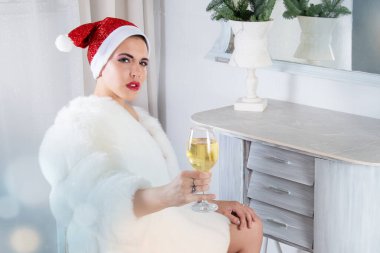 2026 renginde, Noel Baba şapkalı ve kürklü bir kadın bir bardak köpüklü şarap tutuyor. - Şampanya. Noel ve Yeni Yıl 'ın gelişi için şenlikli bir geçmiş