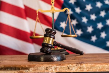 Yargıcın tokmağı, arka planda Birleşik Devletler bayrağı ve adalet terazisi olan bir mahkeme salonundaki ahşap masada. Amerikan demokrasisinde hukuk sistemi, hukuk ve anayasa.