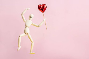 Gülümseyen tahta bir heykel pembe arka planda aşk ve romantizmin sembolü olarak kırmızı bir Karamel Kalp 'i sunar. Sevgililer Günü için tebrik kartı, Anneler Günü, düğün ya da evlilik teklifi..