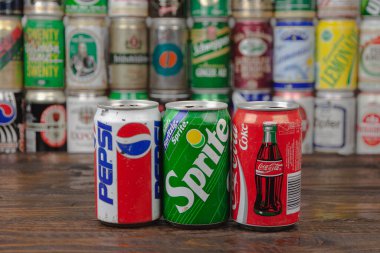 Üç adet Pepsi, Sprite, Coca-Cola alüminyum teneke kutu ve ahşap masa üzerinde bulunan kutular.