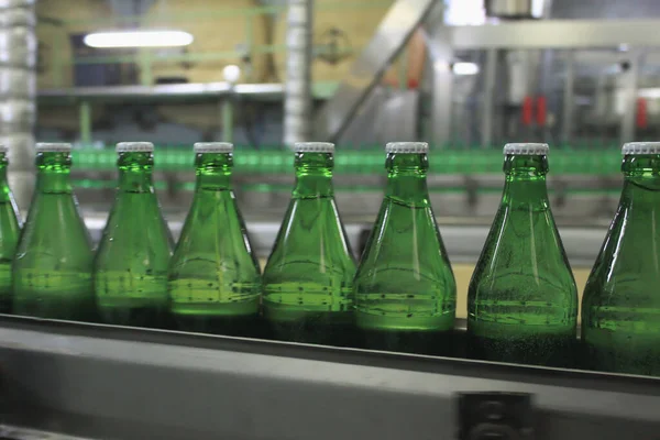 Automatic conveyer belt with green glass bottles for beverages. Concept of producing clean bottled water