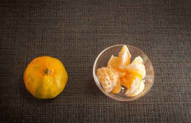 Siyah arka planda taze mandalina soyulmuş. Yakınlarda mandalina dilimleri var. Mevsimlik turunçgiller, doğal sağlıklı yiyecekler. Yakın plan.