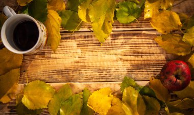 Sarı ve yeşil yapraklı üst görünüm sonbahar kompozisyonu yanmış ahşap zemin üzerinde bir fincan çay ve elma ile birlikte. Üzerinde metin için boş alan var.