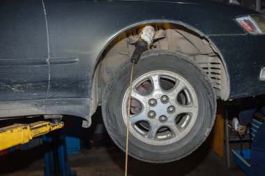 Araba bir oto tamirhanesinde hidrolik asansörde asılı duruyor. Ön tekerleğin üstünde süspansiyonu incelemek için bir ışık var. Araba servisi iş konsepti