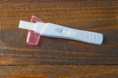 Siyah ahşap arka planda pembe şapkalı beyaz hamilelik testi. Yakın plan.