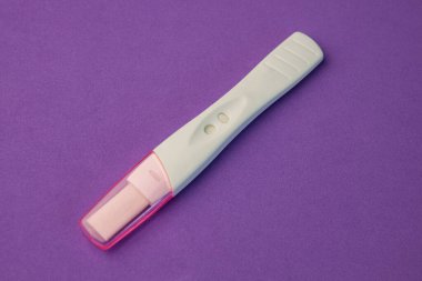 Mor arka planda pembe kapaklı beyaz hamilelik testi. Yakın plan.