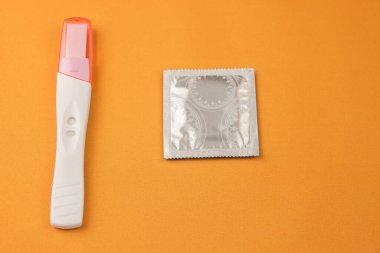 Hamilelik testi ve sarı arka planda bir prezervatif. İstenmeyen hamileliği önleme kavramı. Yakın plan.