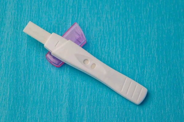 White pregnancy test with a pink cover on light blue background. Close-up