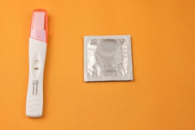 Hamilelik testi ve negatif sonuç sarı arka plandaki bir prezervatiftir. İstenmeyen hamileliği önleme kavramı. Yakın plan.