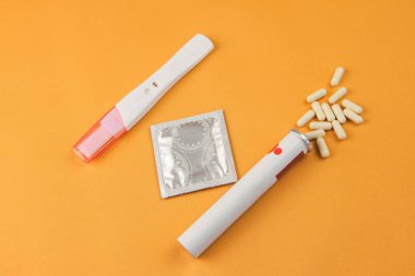 Negatif sonuç veren bir hamilelik testi, sarı arka planda prezervatif ve doğum kontrol hapları. Hamileliğin önlenmesi kavramı