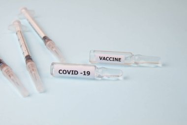 Açık mavi arka planda Covid-19 aşısıyla birlikte şırıngalar ve ampuller var. Yakın plan.