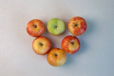 Beş kırmızı ve bir yeşil elma gri arka planda bir üçgen şeklinde uzanır. Yakın plan.