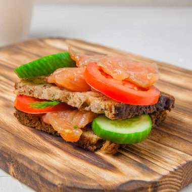 Kırmızı balıklı sandviç, kepekli ekmek, salatalık, otlar ve domatesler köy tahtasında. Sağlıklı yiyecek kavramı