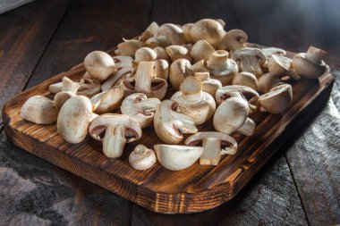 Dilimlenmiş mantarlar, koyu ahşap arka planda yanmış bir kesim tahtasının üzerinde yatar. Yakın plan.