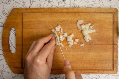 Bir adam doğrama tahtasındaki beyaz soğanları kesmek için bıçak kullanıyor. Üst görünüm