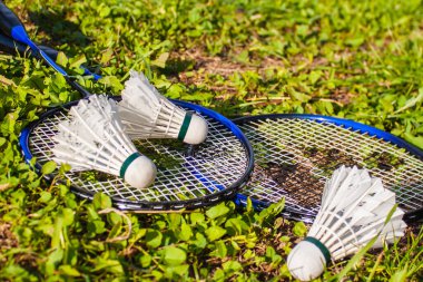 Çimlerin üzerinde iki badminton raketi ve üç mekik horozu var. Yakın plan. Açık hava sporları konsepti