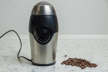 Elektrikli kahve öğütücüsü yanında kavrulmuş kahve çekirdekleri olan beyaz bir masada oturur. Taze demlenmiş kahve kavramı