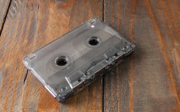 An audio cassette with a transparent dark case. it lies on a brown wooden background. Top view from the side. Close-up