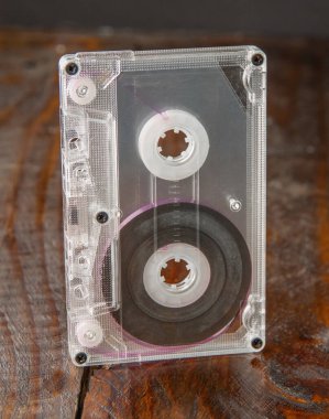 Kahverengi ahşap arka planda, şeffaf çantalı bir ses kaseti dikey duruyor. Yakın plan.