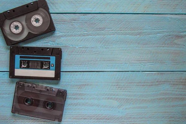 In the left corner of the frame, on a blue wooden background, there are three audio cassettes. On the right, there is an empty space for the text. Top view. Close-up