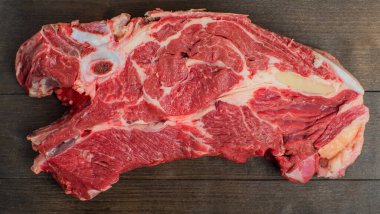 Siyah bir doğrama tahtasının üzerinde kemik ve yağ katmanlı taze bir et parçası var. Yakın plan.