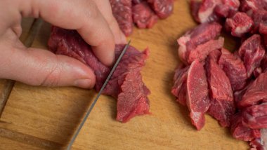 Bir kadın eli ve bir bıçak kesme tahtasının üzerinde sığır etini parçalara ayırdı. Yakın plan.