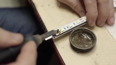 Servis merkezinde, lehim demiriyle bir adamın eli LED arka lambasını tamir ediyor. Yakında duman var.