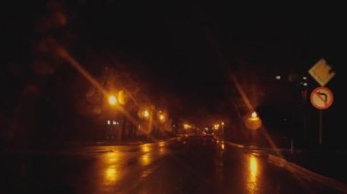 Overnight car ride in the rain. Yellow city lights, glare, passing cars, drops on the windshield. Working wipers