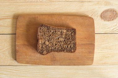 A slice of dark rye bread sits on a small cutting board that sits on a wooden background. Top view
