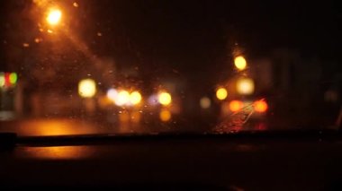 Arabayla gece gezisi. Yağmur yağıyor, silecekler çalışıyor. Ön cama odaklan. Gerisi bulanık.
