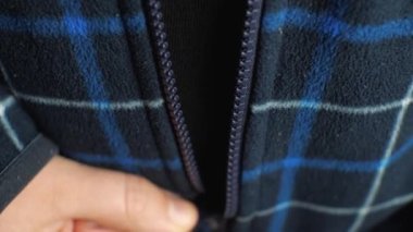 Bir el ekose ceketin plastik fermuarını kapatır. Yakın plan.