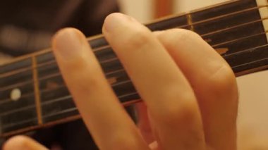 Bir adamın parmakları yıpranmış bir akustik gitarın tellerinde zıplıyor. Yakın plan.