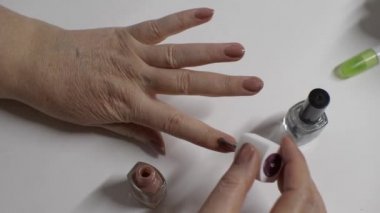 Yaşlı bir kadın kendine pullu kahverengi vernikli manikür yapar. Beyaz arka plan. Parmaklarına yakın çekim. Vücut Bakımı Konsepti