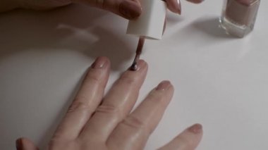 Bir kadının eli, tırnaklarını pullu kahverengi ojeyle boyar. Beyaz arka plan. Parmaklarına yakın çekim. Vücut Bakımı Konsepti