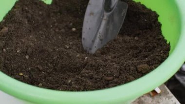 Çiçekler için toprağı olan yeşil bir leğen ve masada bir spatula var. Kamera aşağıdan yukarıya hareket ediyor. Bahçe konsepti