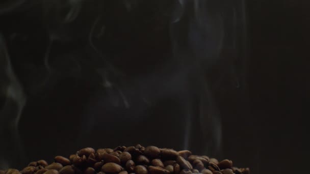 更多的咖啡豆落在上面的一把咖啡豆上 整个画面笼罩在浓烟之中 新鲜烤咖啡的概念 黑色背景 — 图库视频影像