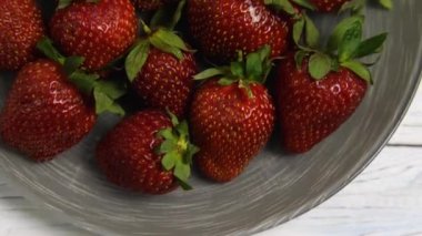 Yeşil yapraklı taze kırmızı çilekler tabakta yatıyor. Kameranın Vvurkh 'un aşağısındaki hareketi. Yakın plan.