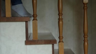 Kot pantolonlu ve beyaz çoraplı ayaklar ahşap bir merdivenin basamaklarından iniyor. Kamera kenarda sabit duruyor. Yavaş çekim