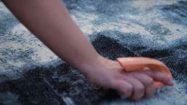 Halıyı elle yıka. Bir kadının eli turuncu bir fırçayla halının yüzeyini fırçalar. Yavaş çekim. Yakın çekim.
