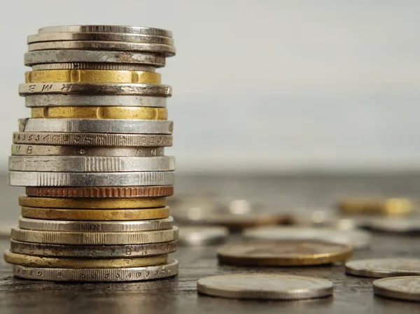 Farklı ülkelerin paraları üst üste bir kule şeklinde istiflenmiştir. Diğer madeni paralar siyah arkaplana saçılmış. Tasarruf kavramı. Yakın plan.