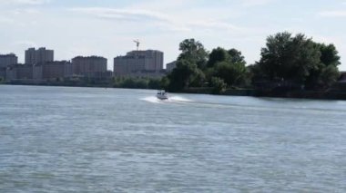 Bir motorlu tekne akıntıya karşı şehrin arka planına karşı nehirde yüzer. Şehir manzarası. Sabit çerçeve